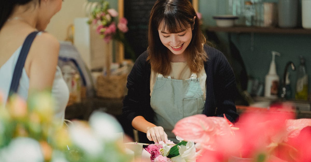 Content Asian female florist wearing light green apron composing tender bouquet for positive female customer while working at counter in floristry shop